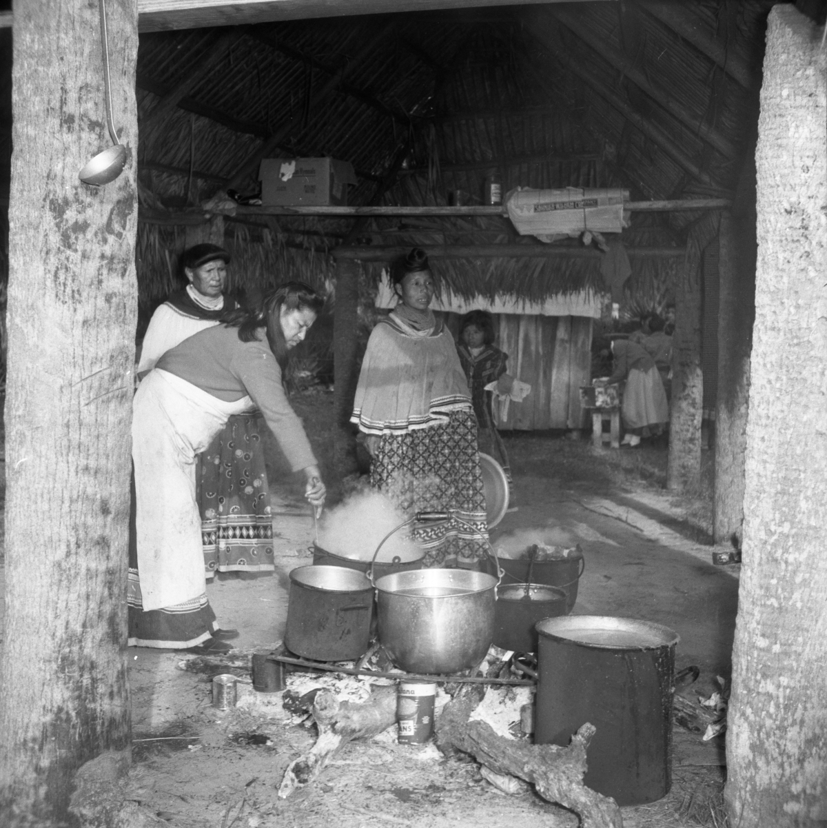 Seminole women standing in front of several cooking pots