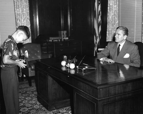 Governor Fuller Warren posing at the desk for junior photographer