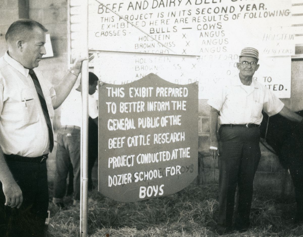 School superintendent Lenox Williams, left, and herdsman B.M. Townsend standing next to an exhibit sign at the Florida School for Boys in Marianna, Florida.