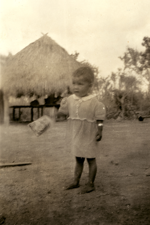 Portrait of a Seminole child near chickees at a village on the Tamiami Trail.