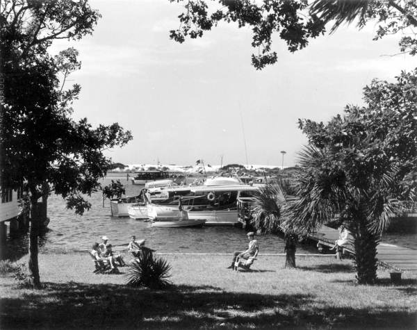 Cruise members rest on the lawn of the Miramar hotel with boats anchored in the background