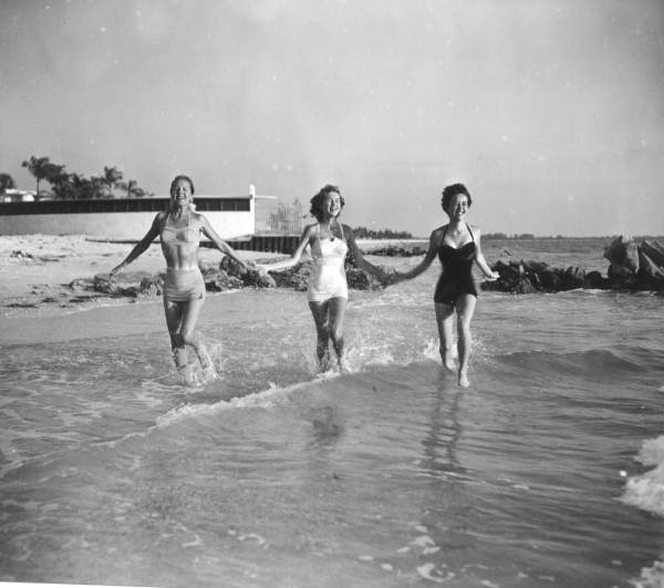 Young women run hand in hand in the surf.