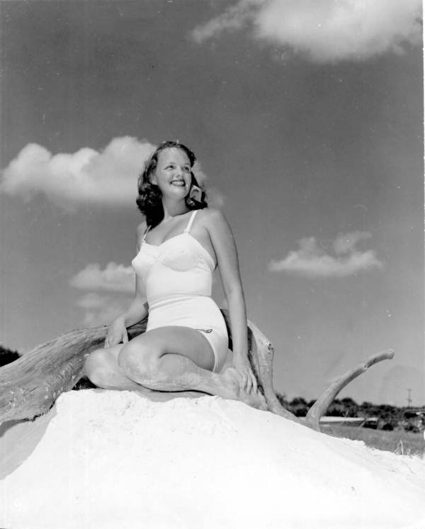 Young woman posing on sand heap with driftwood.
