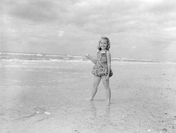 A girl holding a seashell stands on the beach at Sanibel-Captiva Islands - Lee County, Florida.