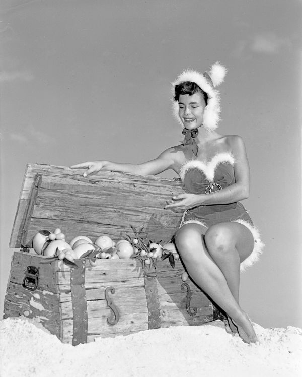 Gloria Howard dressed in Christmas outfit sitting on a chest of fruit