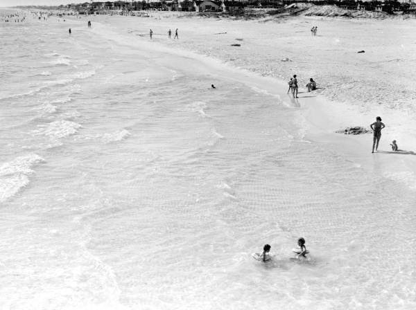 Children wading in the water with people watching from the beach.