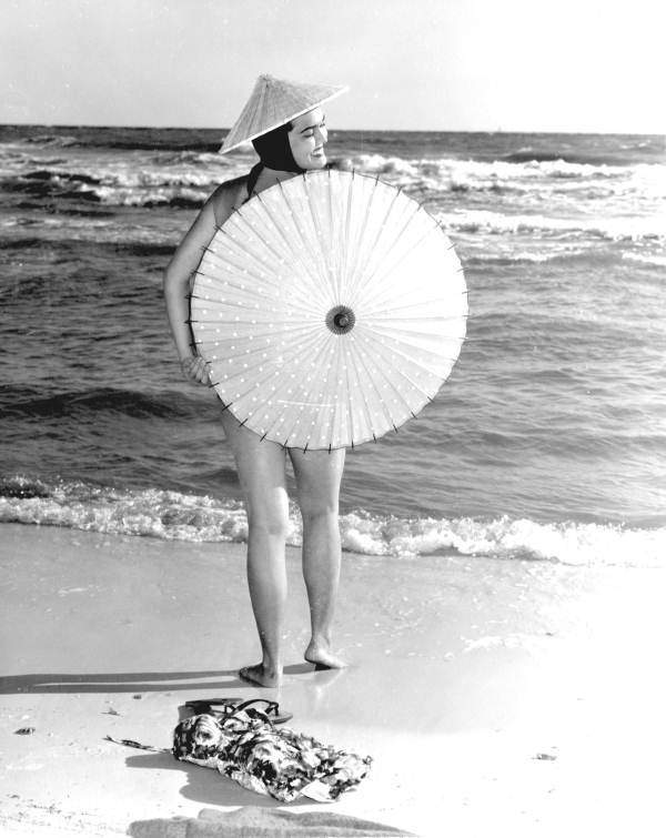 Pat Finn poses on the beach barely covering her body with an umbrella.