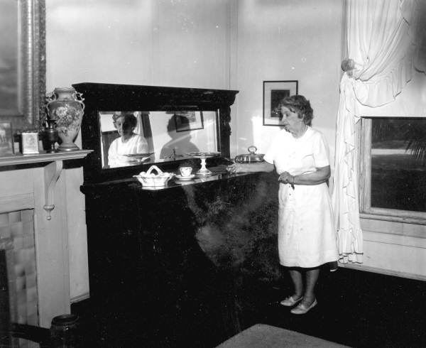 Alice Parlin Hodges stands next to an antique sideboard in her dining room - Apalachicola, Florida.