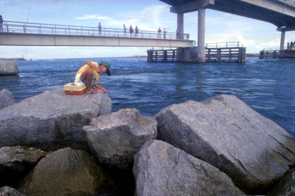 View showing a boy fishing from jetty near bridge at Sebastian Inlet State Park - Melbourne Beach, Florida.