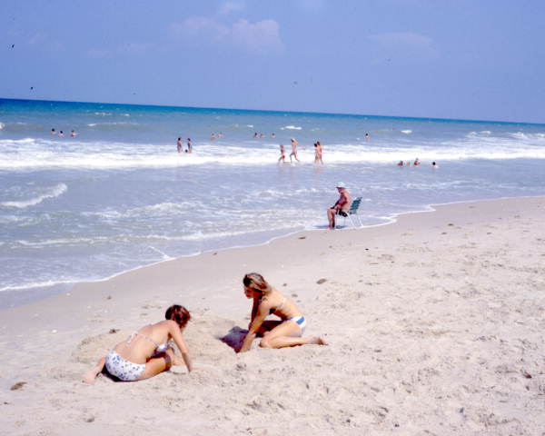 Young women in bikinis digging in the sand at the beach - Melbourne Beach, Florida