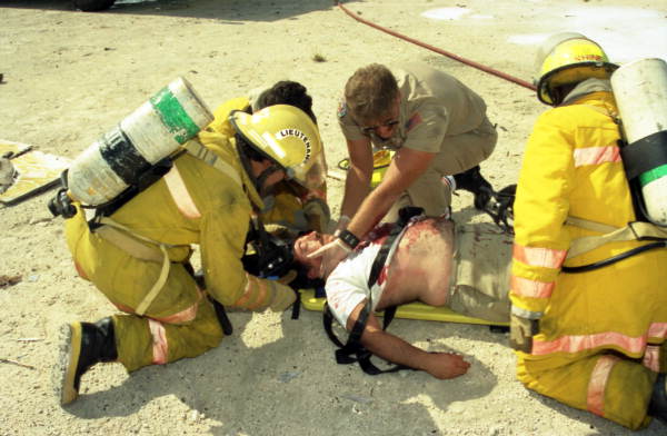 Key West NAS Fire Department firefighters administering simulated first aid to accident victim on a backboard during a vehicle extrication class at the hot drill training area.