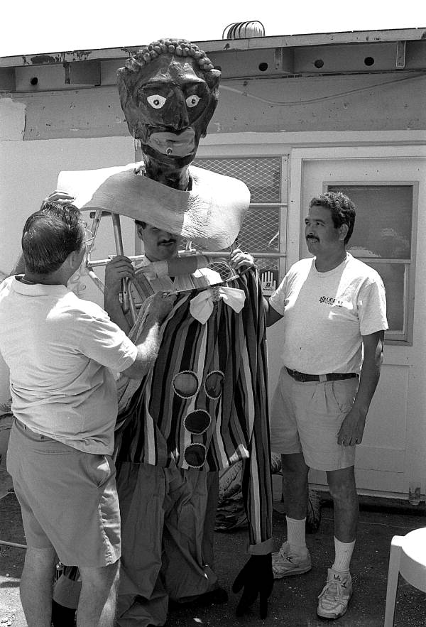 Isaac Duenas (L) and apprentice Ramon Zepeda putting gigante costume onto Isaac's son David - North Miami Beach, Florida.