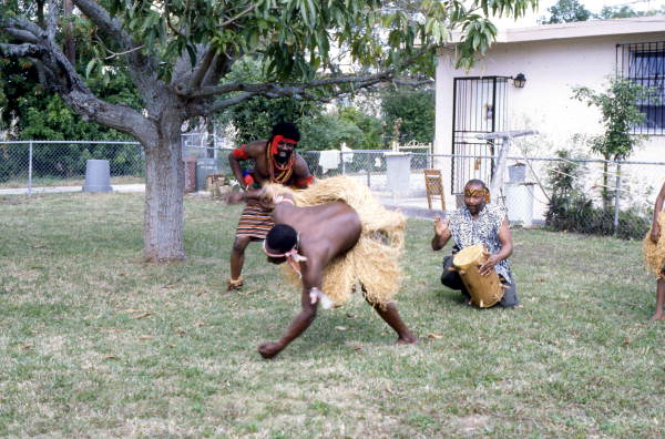 Nigerian acrobatic dancer Felix Omeben performs as Augustine Omeben looks on and Moses Campbell drums - North Miami, Florida.