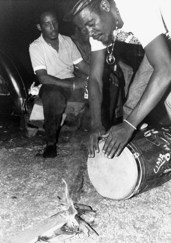 Member of Haitian Rara band Konbo Guinyn tunes his conga drum by heating the head - Miami, Florida.