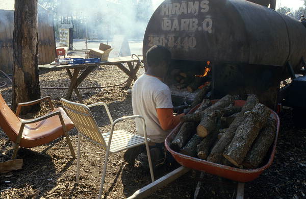 Unidentified African American man putting wood into Hiram Jenkins' barbecue - Jacksonville, Florida
