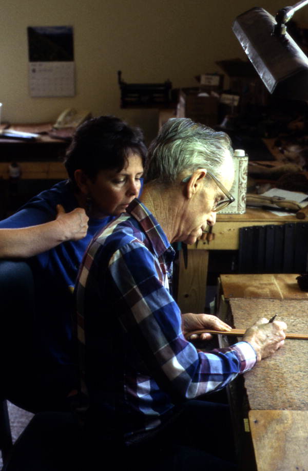 Leather worker Bob Dellis works while apprentice Kitt Maynard looks on - Okeechobee, Florida