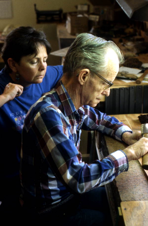 Leather worker Bob Dellis works while apprentice Kitt Maynard looks on - Okeechobee, Florida