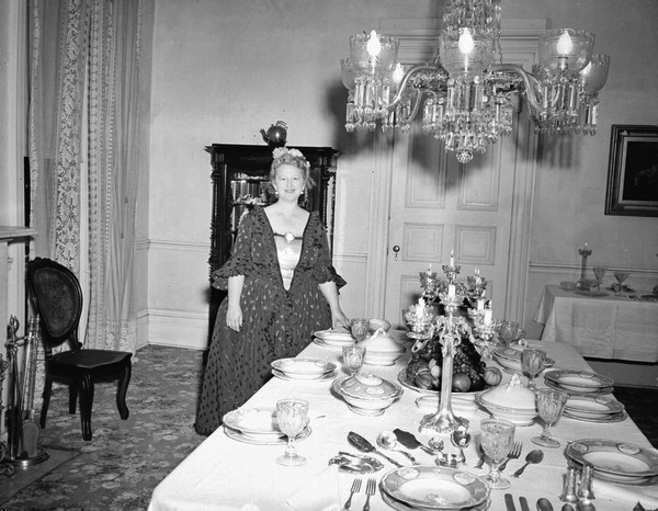 Margaret Hood next to dining room table with tableware and silverware sets on display at Goodwood