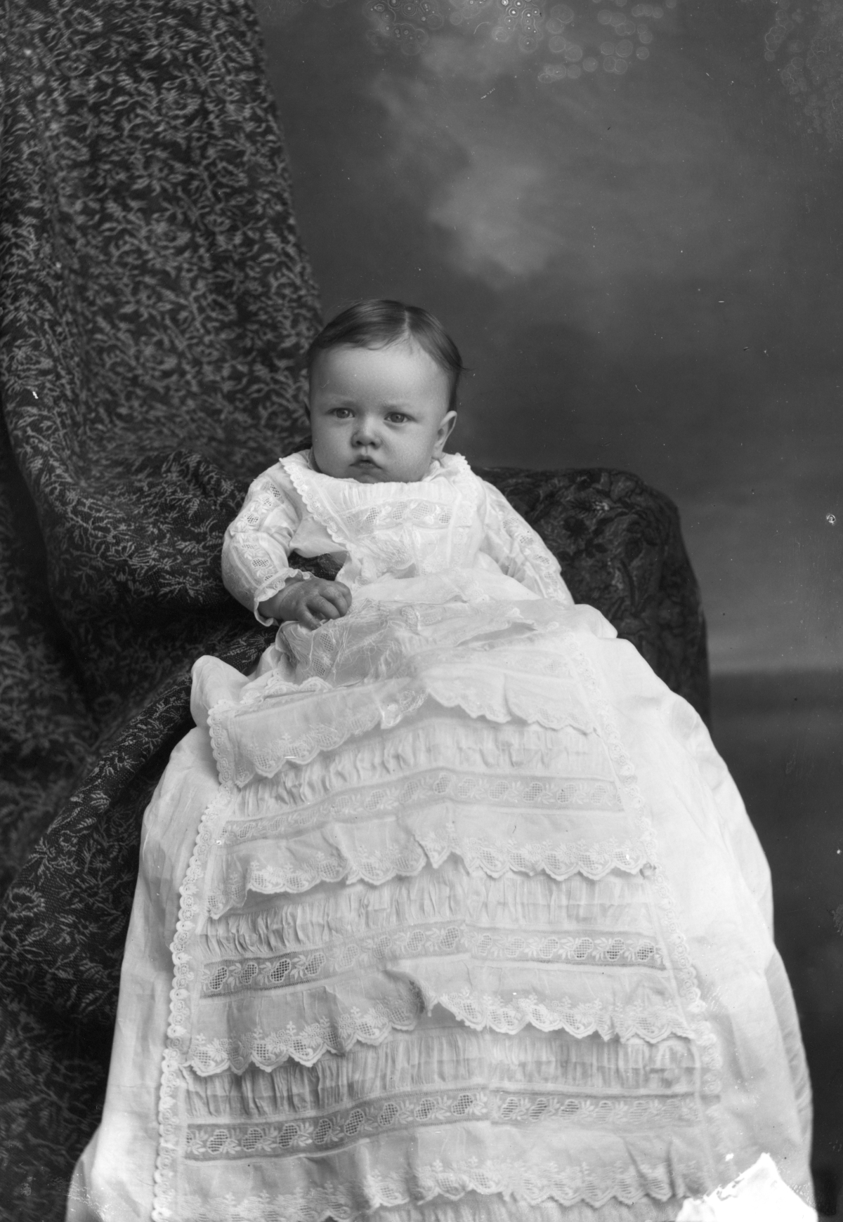 Infant in a long ruffled gown.