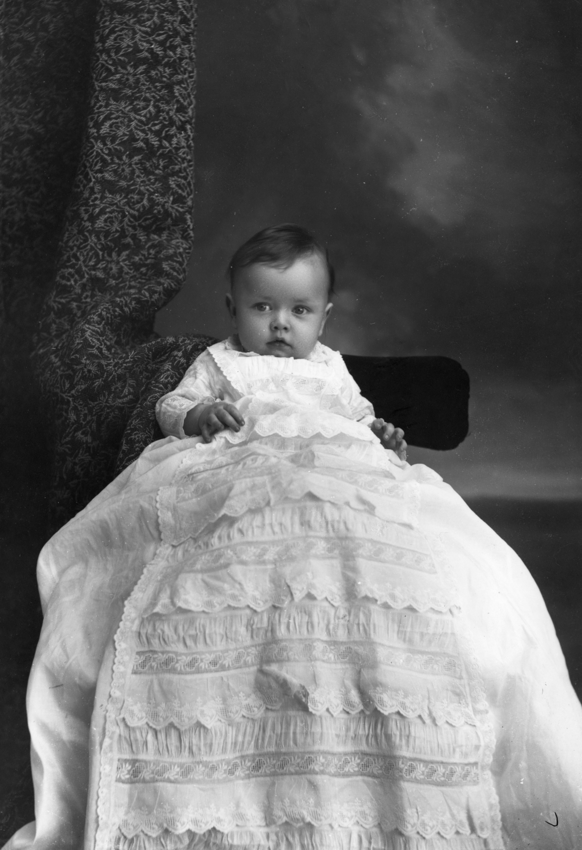 Infant wearing a long ruffled gown.