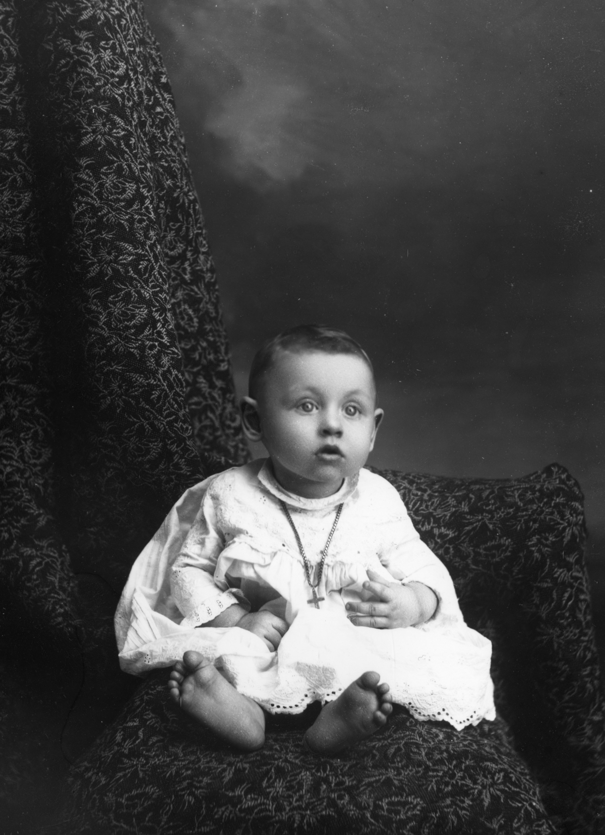 Wide-eyed infant wearing a cross necklace.
