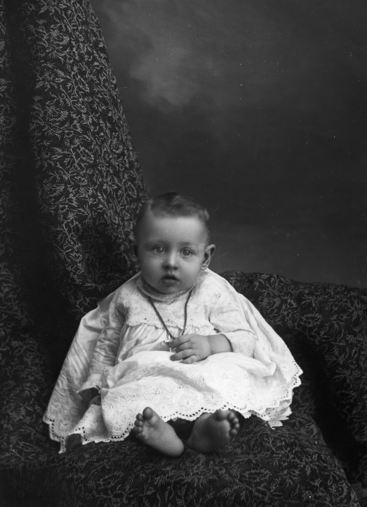Infant holding a cross necklace.