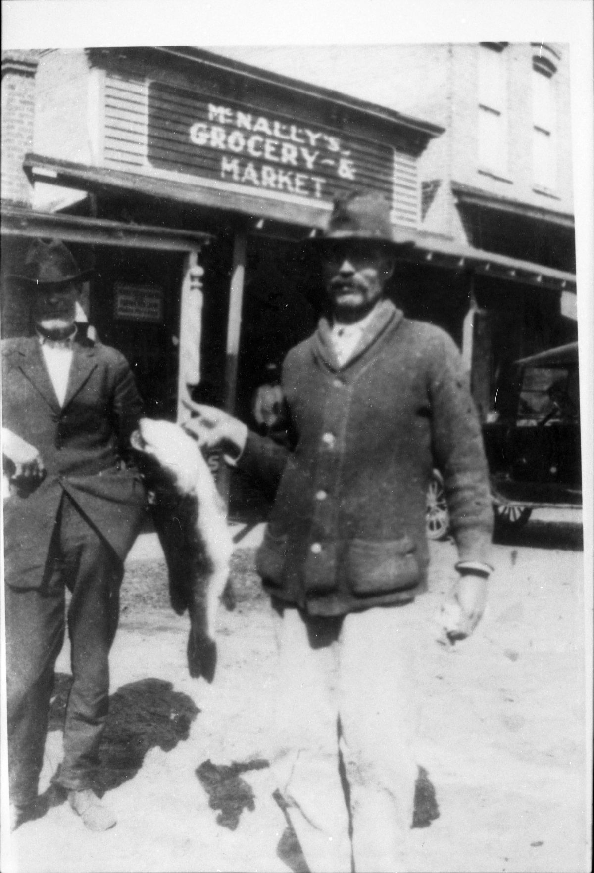 Man holding up bass fish in front of McNally's grocery store - Madison County, Florida