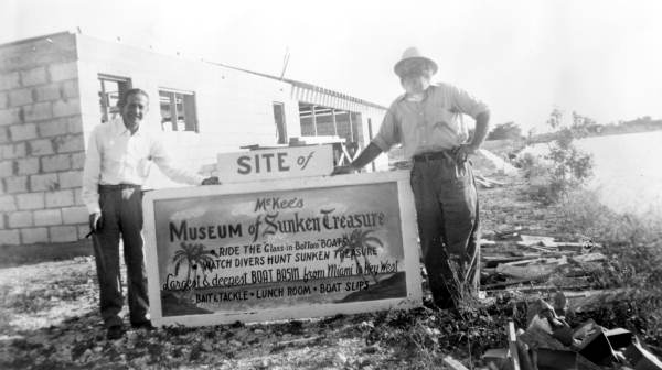 Unidentified men standing next to sign at the construction site of first McKee museum - Plantation Key, Florida