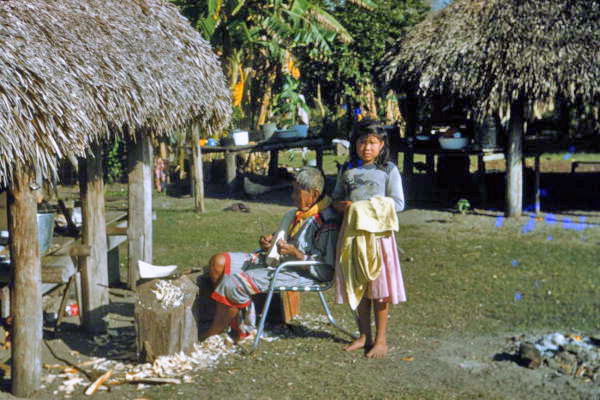 Young Seminole Indian girl by Charlie Cypress as he whittles wood