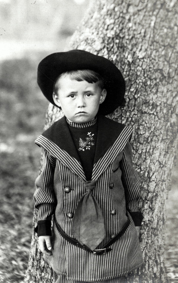 Frowning boy posed in front of tree trunk
