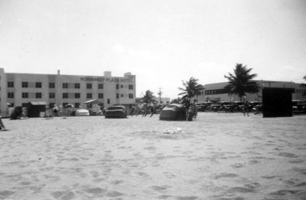 View showing visitors vacationing at the beach near the Normandy Plaza Hotel in Miami Beach, Florida.