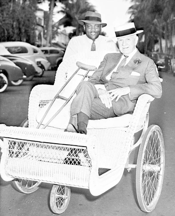 Colonel Edward R. Bradley in a bicycle cart pushed by an African American man.