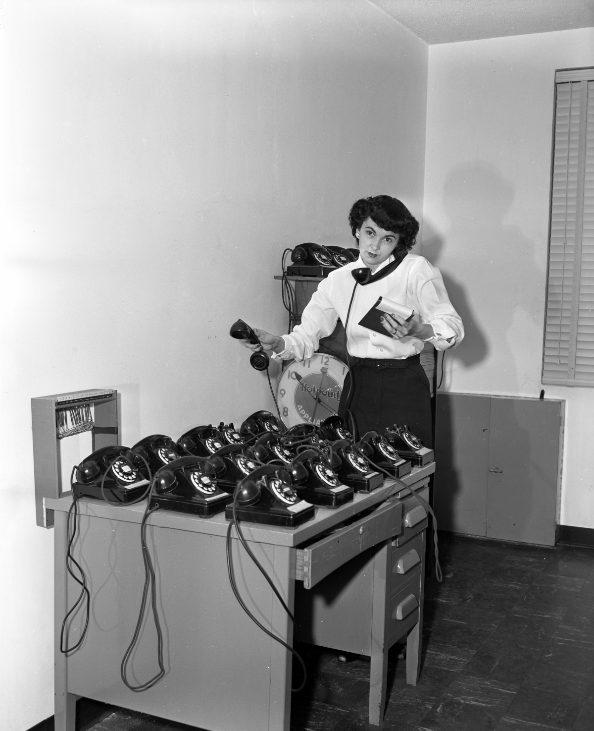 Mrs. Red Taylor with a desk covered with telephones.