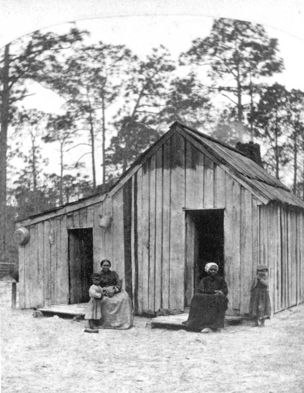 African Americans standing outside wooden house