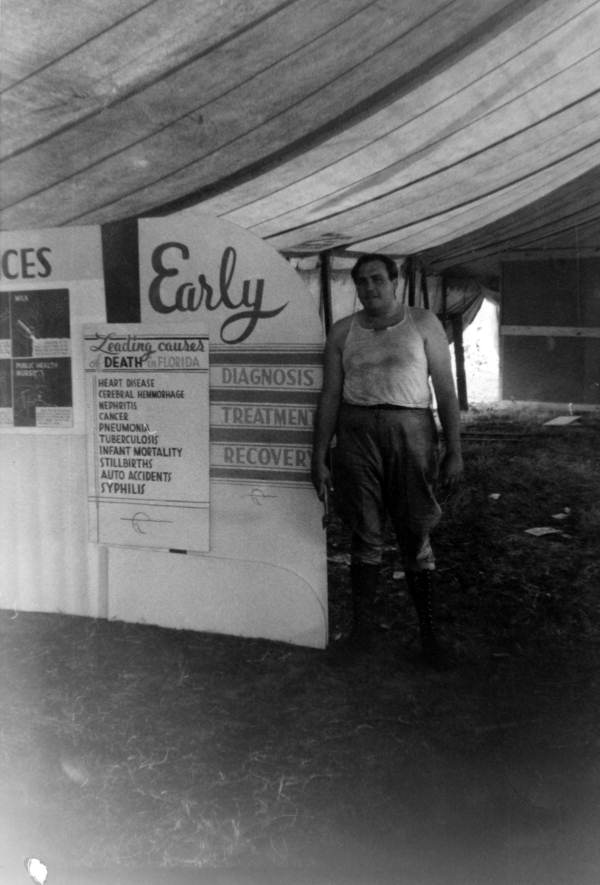 Florida State Board of Health employee standing next to the S.B.H. exhibit at the Highlands County Fair.