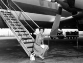 Miss Florida 1965, Carol Blum, sitting on step in front of a passenger plane.