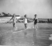 Young women run hand in hand in the surf.