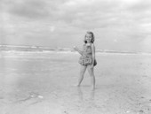 A girl holding a seashell stands on the beach at Sanibel-Captiva Islands - Lee County, Florida.