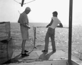 A man watches a young man holding a king mackerel with a gaff in the charter boat - Destin, Florida.