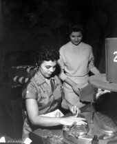A lady watches a woman rolling a cigar in a cigar factory - Tampa, Florida.