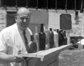 An elderly man standing next to a display of glass and ceramic bottles - Pensacola, Florida.