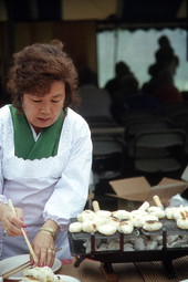 Woman grilling rice cakes for soup during Japanese New Years celebration - Delray Beach, Florida.