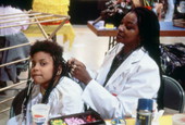 Young girl gets her hair braided .