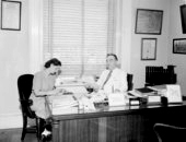Secretary of State R. A. Gray seated at his desk with secretary