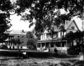 Couple seated on a bench in front of two houses.