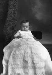 Infant wearing a long ruffled gown.