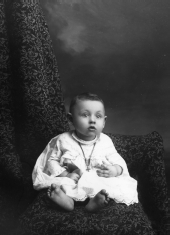 Wide-eyed infant wearing a cross necklace.