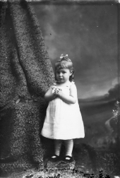 Little girl standing with hands clasped.