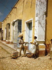 Street vendor holding out onions to a woman holding tropical fruit in Trinidad de Cuba.