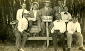 Group portrait of Koreshan men at Bamboo Landing holding sign "Votes for Wimmin".